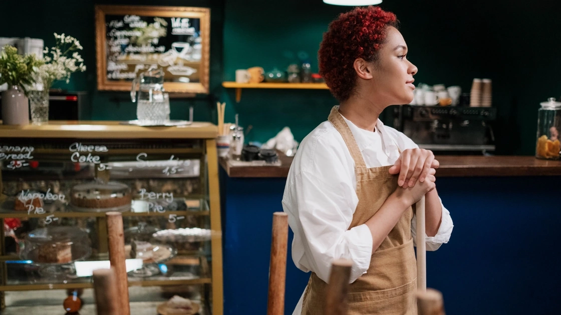 Café owner in an apron leaning on a broom after closing up her shop