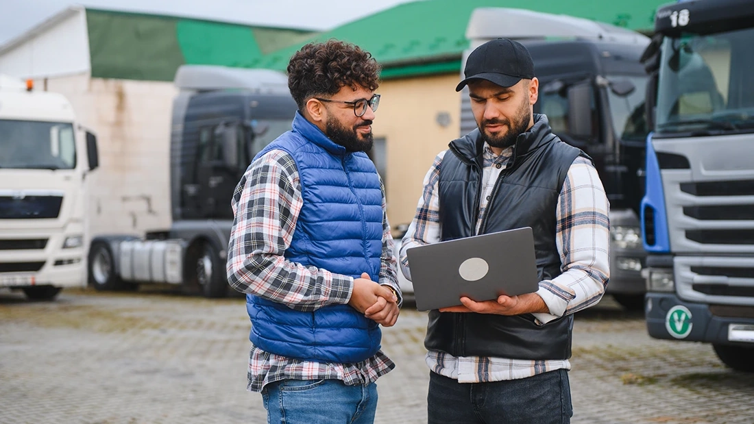 Two fleet owners reviewing a laptop beside trucks