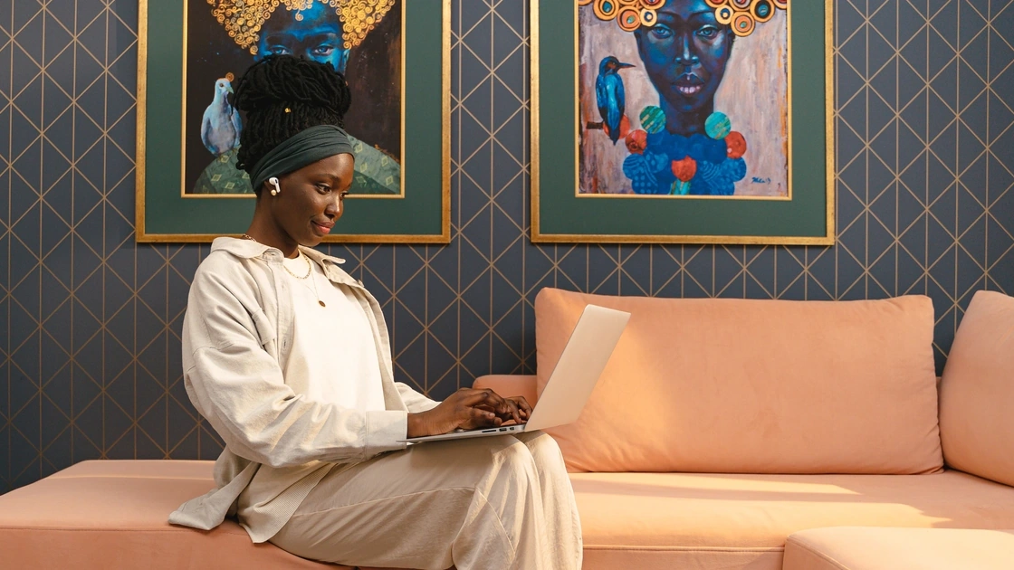 Woman working on a laptop on a peach couch in a modern living room